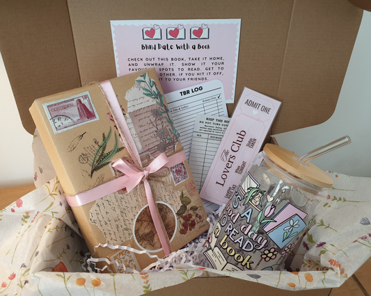 A gift bundle consisting of a hand-wrapped book, a handmade iced coffee cup, bookmarks, a custom TBR list, stickers, decorative page tabs, and a pen or highlighter, all displayed in an open gift box.